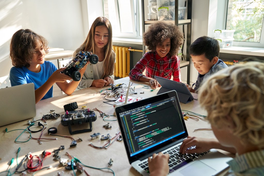 School children students build robotic cars using computers and coding. Happy multiethnic kids learning programming robot vehicles sitting at table at STEM education science engineering class.